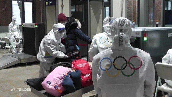Menschen in Schutzanzügen mit Olympia-Logo führen Kontrollen durch. © Screenshot 