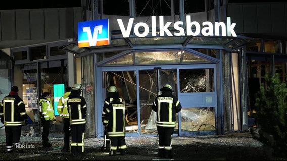 Mehrere Feuerwehrleute stehen vor einer zertrümmerten Volksbankfiliale. © Screenshot 
