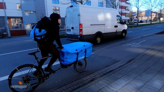 Ein Fahrradkurier fährt mit seinem Lastenrad am Straßenrand auf einem Fahrradschutzstreifen. © Screenshot 