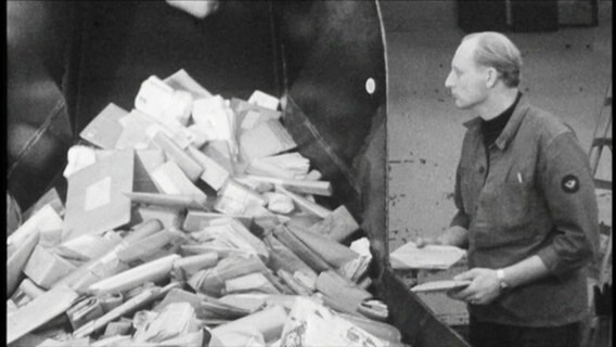 Archivbild: Ein Mann steht neben Briefen und Paketen. © Screenshot 