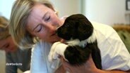 Eine Frau hält einen Hundewelpen in der Hand. © Screenshot 