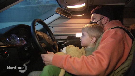Ein Kind sitzt auf dem Schoß seines Vaters in einem Fahrsimulator im Polizeimuseum. © Screenshot 