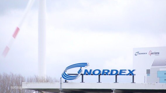 Blick aus der Ferne auf den am Firmengebäude angebrachten Schriftzug der "nordex". Im Hintergrund ein Windrad. © Screenshot 