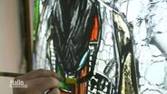Nahaufnahme: Ein Hand malt mit einem Pinsel ein Kirchenfenster an. © Screenshot 