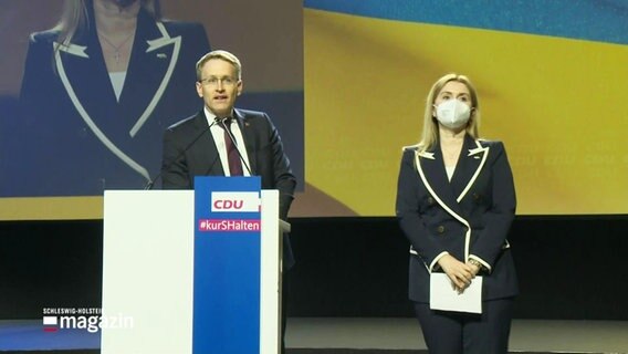 Daniel Günther spricht auf einer Bühne, hinter ihm sieht man die Ukrainiche Nationalflagge. © Screenshot 