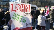 Auf einem Schild einer Streikenden steht die Forderung "Lohn rauf, Kita auf!". © Screenshot 