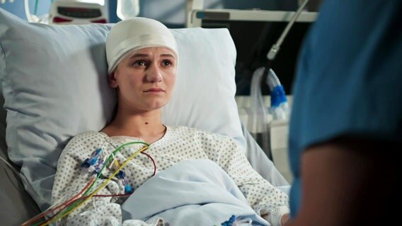Eine junge Frau liegt mit einem Kopfverband in einem Krankenhausbett. © Screenshot 