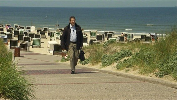 Ein Mann mit Aktentasche läuft an einer Strandpromenade. © Screenshot 