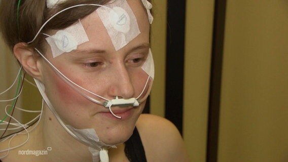 Eine junge Frau mit Elektroden an Hals und Kopf. © Screenshot 