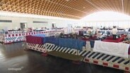 In den Rostocker Messehallen sind mehrere Schlafplätze für GEflüchtete mit Baustellenzäunen abgetrennt. © Screenshot 