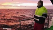 Ein Mann steht an Bord eines Schiffes und schaut aufs Meer. © Screenshot 