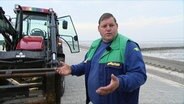 Enno König am Strand. Er steht vor einem Traktor mit dem er die Strandkörbe bewegt. © Screenshot 