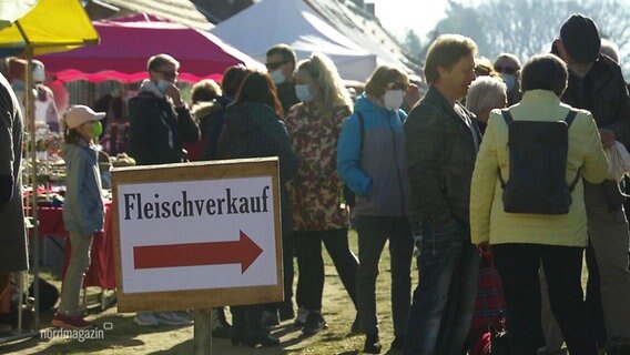 Menschen stehen in einer Schlange, neben ihnen ein Schild mit der Aufschrift:"Fleischverkauf" © Screenshot 