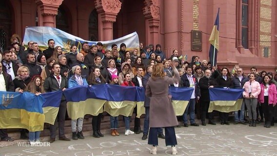 Zusammenstehende Menschen halten ukrainische Flaggen in der Hand und singen. © Screenshot 