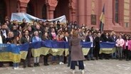 Zusammenstehende Menschen halten ukrainische Flaggen in der Hand und singen. © Screenshot 