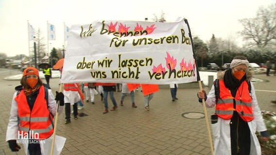 Dermonstrierende Ärztinnen halten einen Banner hoch auf dem dem zu lesen ist: Wir brennen für unseren Bereuf, aber wir lassen uns nicht verbrennen". © Screenshot 