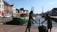 Eine Statue steht an einem kleinen Hafen. © Screenshot 