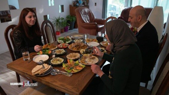 Drei Menschen an einem voll gedeckten Tisch mit verschiedenen Speisen. © Screenshot 