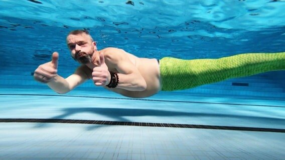 Ein Mann beim Meerjungfrauenschwimmer unter Wasser. © Screenshot 