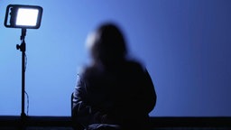 Eine anonymisierte Frau sitzt vor einem Scheinwerfer und gibt ein Interview. © Screenshot 