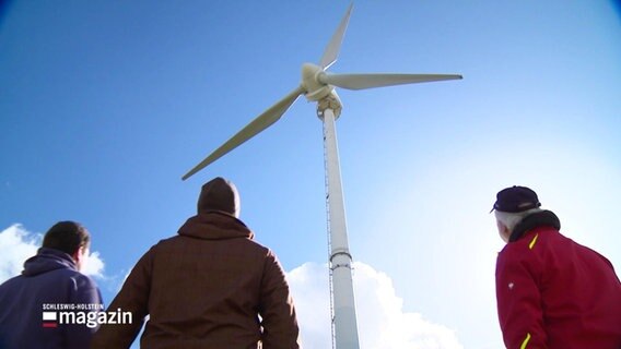 Drei Personen betrachten eine Windkraftanlage. © Screenshot 