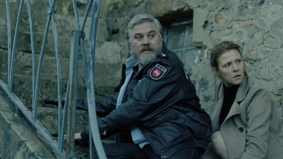 Koops (Aljoscha Stadelmann) und die Personenschützerin Claudia Böhm (Franziska Weisz) hocken angespannt auf einer Steintreppe. © Screenshot 