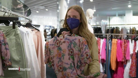 Modeexpertin Leonie Heilig hält ein geblümtes Kleid in die Kamera, dass sie aus der Auslage eines Geschäfts genommen hat. © Screenshot 