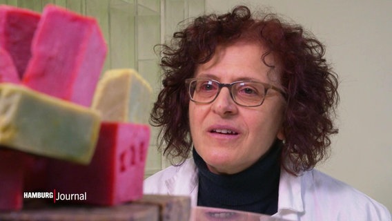 eine lockige Frau mit Brille betrachtet einen Stapel Seifen © Screenshot 