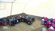 Schulranzen stehen nach Farben platziert in einem Zelt auf einem gemeinnützigem Schulranzen-Fest. © Screenshot 