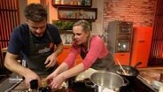 Ein Mann und eine Frau stehen an einer Kochinsel in einem Studio. © Screenshot 