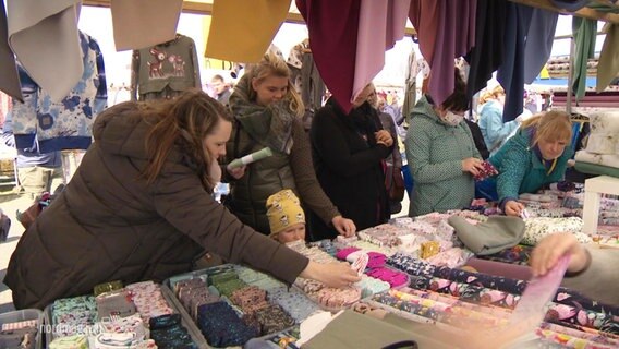 Mehrere Frauen sehen sich die Auslage auf einem Stoffmarktstand an © Screenshot 