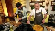 ZWei Männer in Kochschürzen stehen am Herd und kochen © Screenshot 