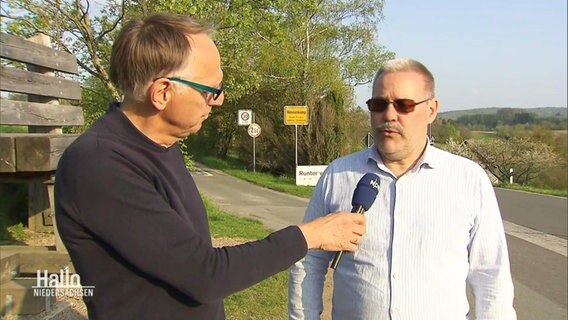 Ein Mann wird vor einem Ortseingangschild interviewt. © Screenshot 