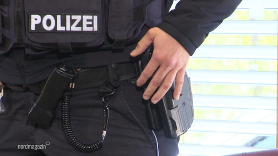 Großaufnahme einer Polizeiuniform, mit kugelsicherer Weste und Holster, eine Hand liegt auf der Dienstwaffe. © Screenshot 