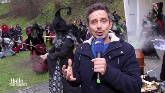 Reporter Peter Jagla berichtet über die Waldpurgisnacht im Harz. Hinter ihm tanzen einige als Hexen verkleidete Menschen. © Screenshot 