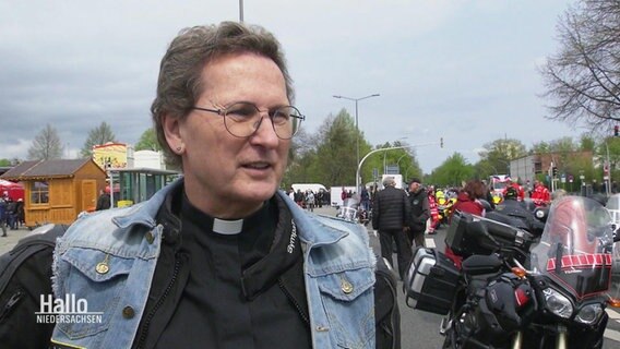 Pfarrerin Marlen Below gibt ein Interview. Sie trägt ihre schwarze Arbeitskleidung als Pfarrerin und darüber eine Biker-Kutte aus Jeans. © Screenshot 