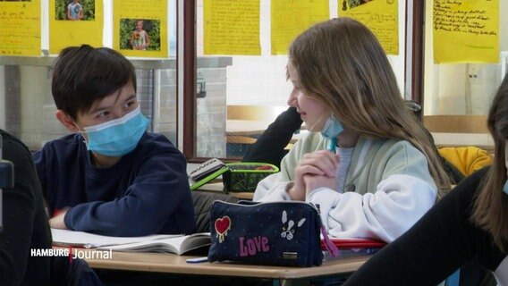 Ein Junge mit Maske und ein Mädchen ohne Maske im Unterricht. © Screenshot 