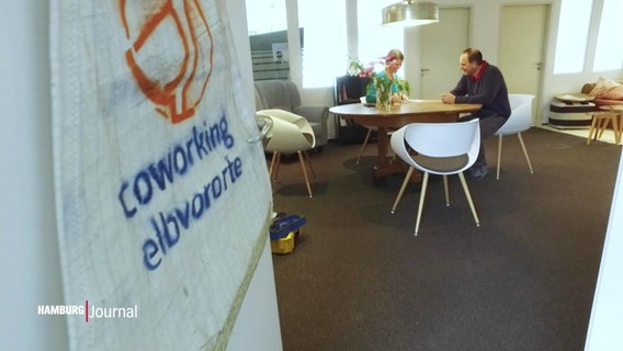 Links im Bildvordergrund das Logo und der Schriftzug von "Coworking Elbvororte", im Hintergrund zwei Personen in einem Raum mit rundem Holztisch und Stühlen. © Screenshot 