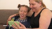 Tetyana Novakova (re.) und ihre Tochter Anastasija sitzen gemeinsam auf einem Sofa und schauen sich etwas auf dem Smartphone an. © Screenshot 