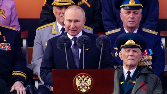 Wladimir Putin hält eine Rede, im Hintergrund mehrere alte Männer in Uniform. © Screenshot 