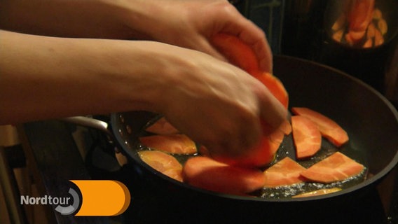 Hände legen geschnittene Karotten in eine Bratpfanne. © Screenshot 