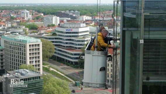 Von einem hängenden Korb aus, putzen zwei Männer Fenster. © Screenshot 