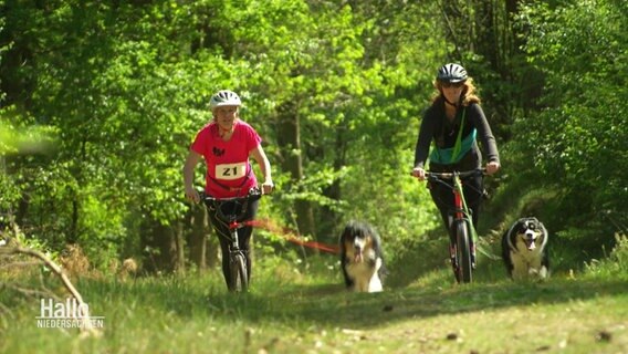 Zwei Fahrradfahrerinnen nehmen mit ihrem Hund an einem Triathlon teil. © Screenshot 