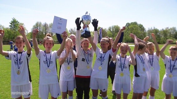 Eine Mädchen-Fußballmannschaft hält stolz einen Pokal und eine Urkunde in die Höhe. © Screenshot 