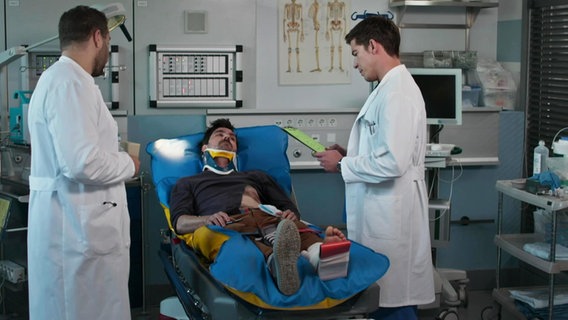 Zwei Ärzte behandeln einen Mann mit gebrochenem Fuß. © Screenshot 