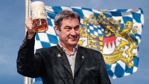 Der bayrische Ministerpräsident Markus Söder mit einem Maßkrug vor der bayrischen Landesflagge.  