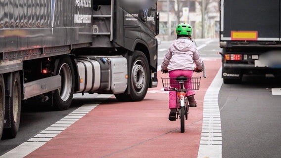 Ein Lastwagen kreuzt einen Fahrradweg, auf dem ein Kind fährt.  