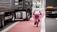 Ein Lastwagen kreuzt einen Fahrradweg, auf dem ein Kind fährt.  