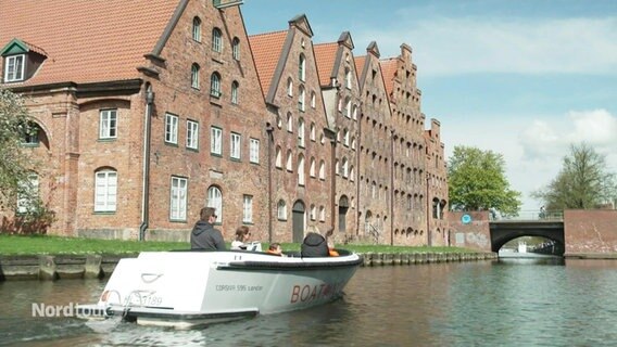 Eine Familie sitzt in einem E-Boot und schippert auf einem Kanal in Lübeck an alten Speichern vorbei. © Screenshot 