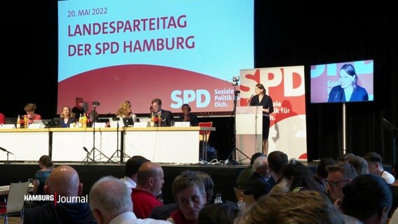 Mehrere Delegierte sitzen vor einer Bühne mit RednerInnen beim Landesparteitag der SPD Hamburg. © Screenshot 
